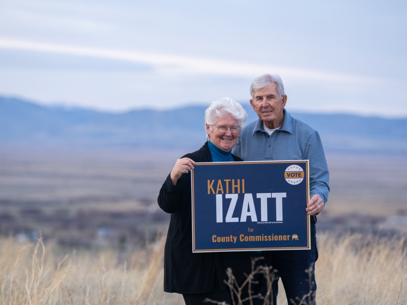 Kathi and Ed Izatt together holding a campaign sign with mountains behind them